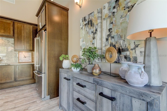 room details with light wood-style flooring, brown cabinetry, backsplash, and freestanding refrigerator