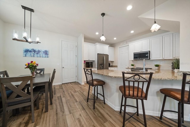 kitchen with white cabinets, light stone counters, a breakfast bar, stainless steel appliances, and pendant lighting