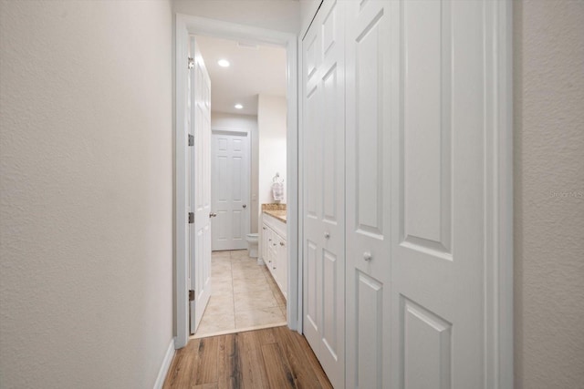 hallway with light wood-type flooring, a textured wall, baseboards, and recessed lighting