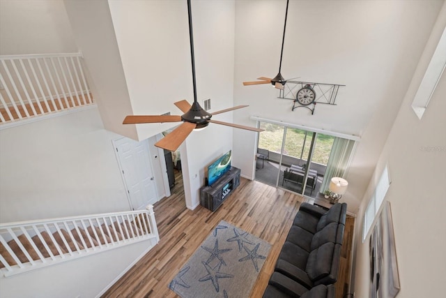 living room featuring a towering ceiling, light wood finished floors, and ceiling fan