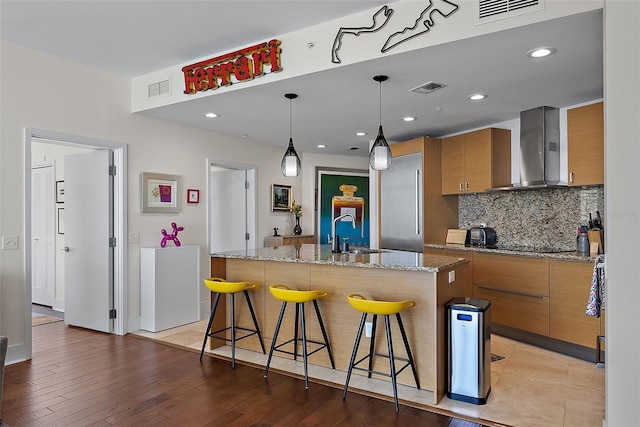 kitchen with brown cabinetry, visible vents, a sink, and wall chimney exhaust hood