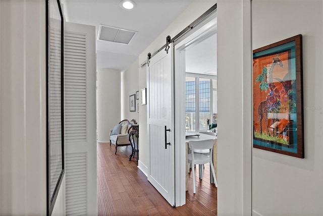 corridor featuring a barn door, wood finished floors, and visible vents