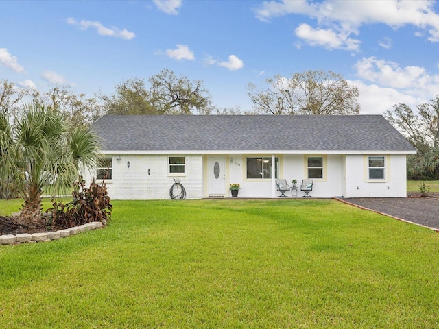 ranch-style house featuring a porch, a front yard, roof with shingles, and brick siding