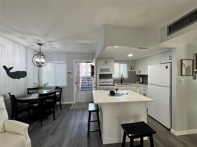 kitchen with hanging light fixtures, dark wood-type flooring, white appliances, a center island, and white cabinetry