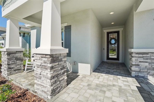 doorway to property with stucco siding, a porch, and stone siding