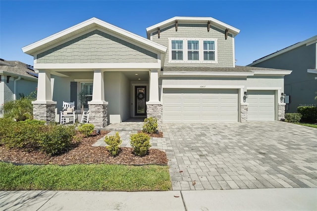 craftsman inspired home featuring a porch, stone siding, an attached garage, stucco siding, and decorative driveway