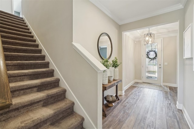 entryway featuring wood finished floors, ornamental molding, baseboards, stairs, and a notable chandelier