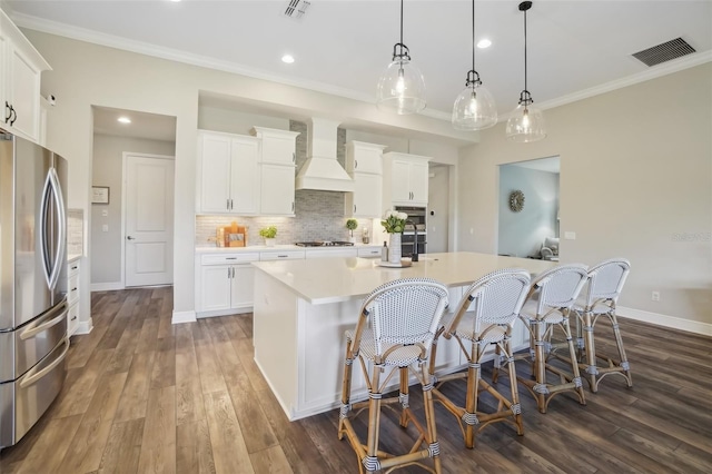 kitchen featuring crown molding, light countertops, custom range hood, appliances with stainless steel finishes, and visible vents