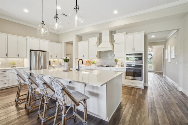 kitchen with a large island with sink, backsplash, ornamental molding, premium range hood, and appliances with stainless steel finishes
