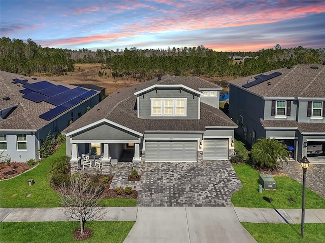 view of front of house with decorative driveway, a lawn, stone siding, a garage, and roof with shingles