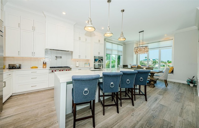 kitchen featuring tasteful backsplash, decorative light fixtures, crown molding, white cabinetry, and a kitchen island with sink