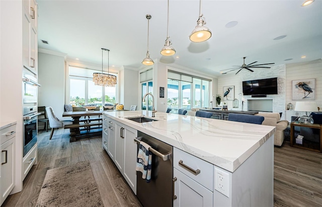 kitchen featuring white cabinetry, a center island with sink, sink, stainless steel dishwasher, and pendant lighting