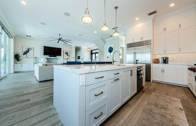 kitchen featuring sink, light stone counters, white cabinetry, hanging light fixtures, and an island with sink