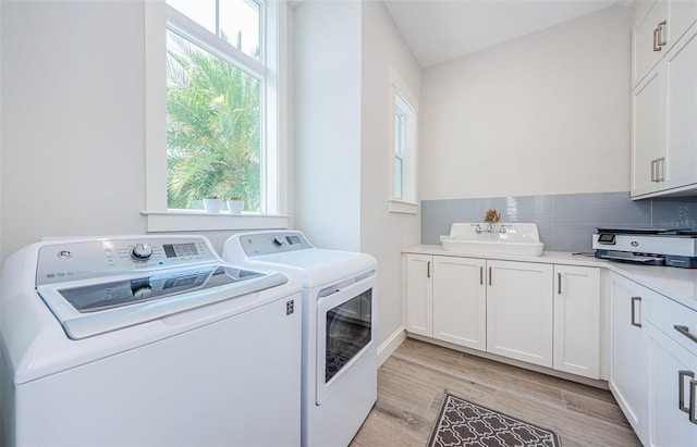 clothes washing area featuring independent washer and dryer, a wealth of natural light, sink, and light hardwood / wood-style flooring