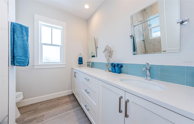 bathroom with hardwood / wood-style floors, backsplash, vanity, tiled shower, and toilet