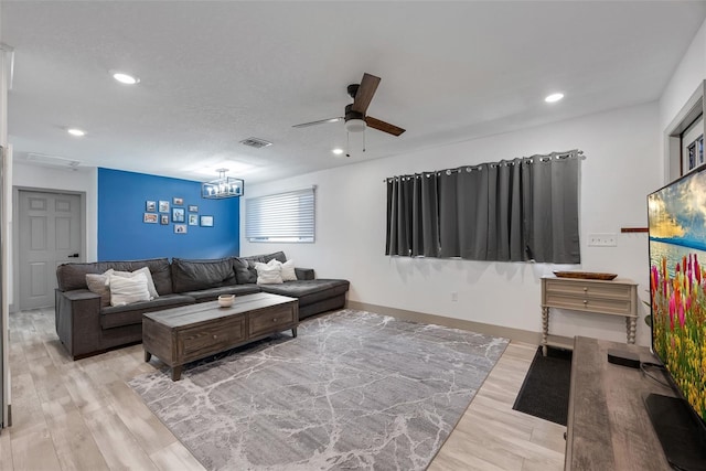 living room with ceiling fan with notable chandelier and light hardwood / wood-style floors