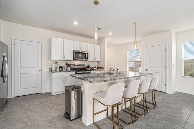 kitchen with a sink, visible vents, white cabinets, appliances with stainless steel finishes, and dark stone counters