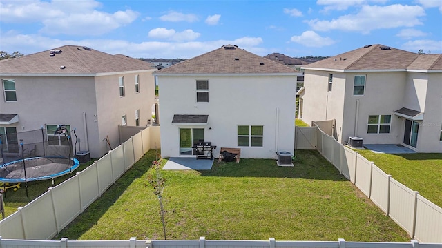 rear view of property with a fenced backyard, central AC, a lawn, stucco siding, and a trampoline