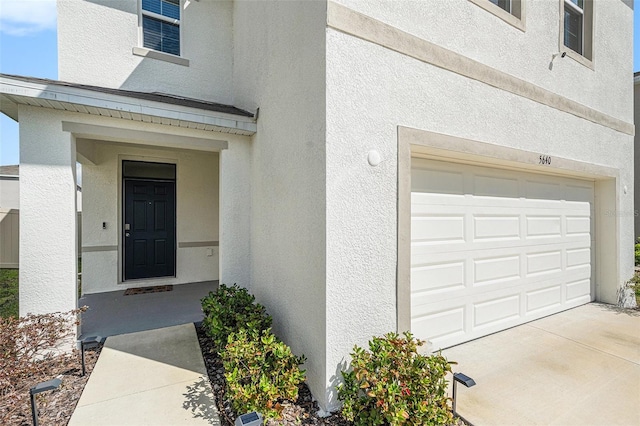 doorway to property featuring concrete driveway, an attached garage, and stucco siding