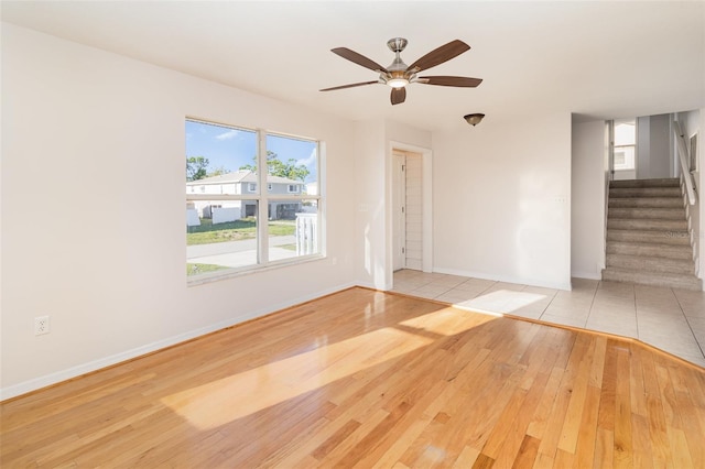 unfurnished room with stairway, a ceiling fan, baseboards, and wood-type flooring