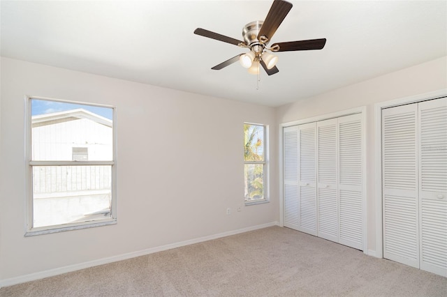 unfurnished bedroom with baseboards, multiple closets, light colored carpet, and a ceiling fan