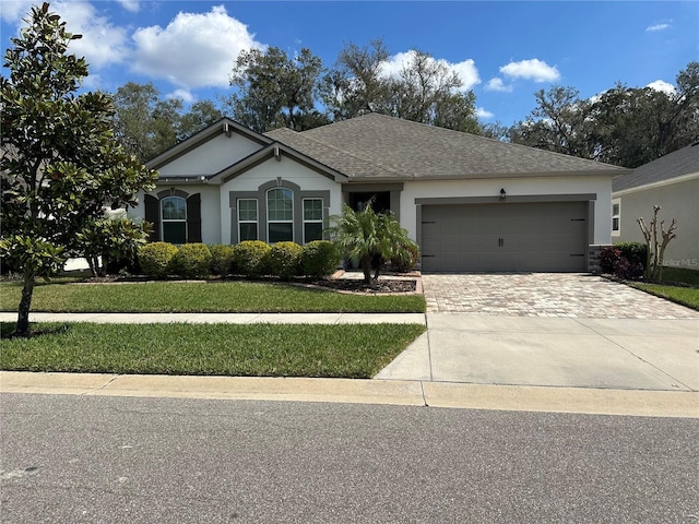 ranch-style house with a front lawn, decorative driveway, an attached garage, and stucco siding