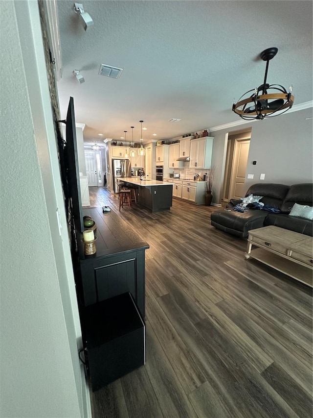 living room featuring a textured ceiling, dark wood finished floors, visible vents, and crown molding