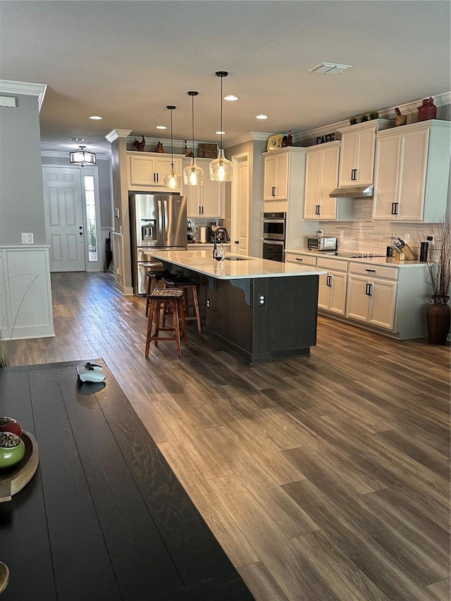 kitchen with decorative light fixtures, a center island with sink, stainless steel refrigerator with ice dispenser, light countertops, and a sink