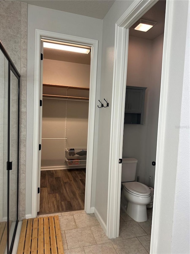 bathroom with wood finished floors, a walk in closet, and toilet