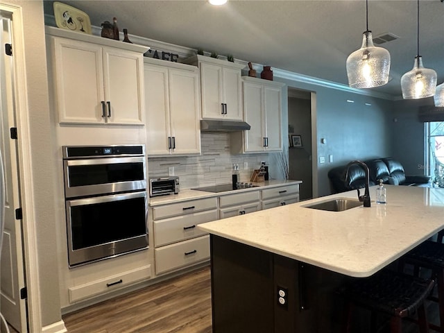 kitchen featuring hanging light fixtures, black electric stovetop, a sink, and a kitchen island with sink