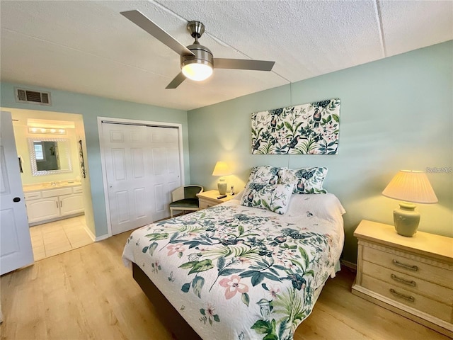 bedroom with a textured ceiling, visible vents, a closet, light wood finished floors, and ensuite bath