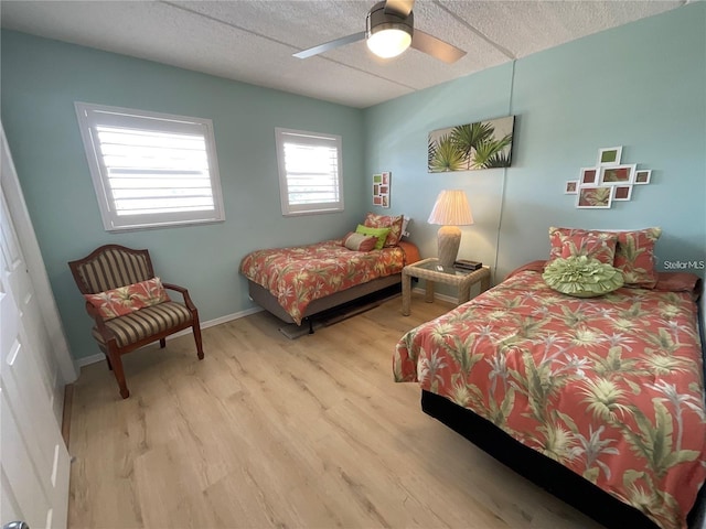 bedroom featuring a ceiling fan, a textured ceiling, baseboards, and wood finished floors