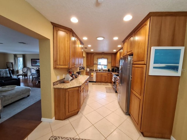 kitchen featuring light tile patterned floors, brown cabinets, open floor plan, stainless steel appliances, and pendant lighting