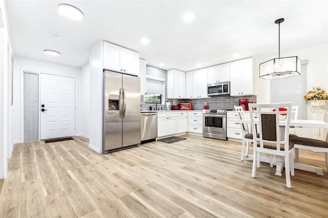 kitchen with appliances with stainless steel finishes, light hardwood / wood-style flooring, decorative light fixtures, sink, and white cabinetry