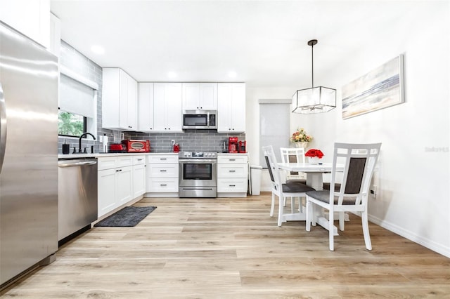 kitchen featuring stainless steel appliances, white cabinets, pendant lighting, backsplash, and light wood-type flooring