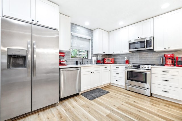 kitchen with backsplash, white cabinets, stainless steel appliances, and light hardwood / wood-style floors