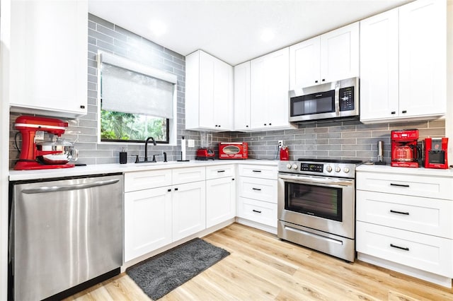 kitchen featuring sink, light wood-type flooring, white cabinetry, stainless steel appliances, and tasteful backsplash