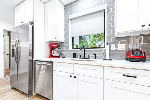 kitchen with sink, white cabinetry, light hardwood / wood-style floors, stainless steel appliances, and decorative backsplash