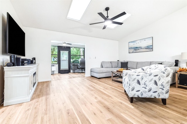 living room with vaulted ceiling with skylight, light hardwood / wood-style flooring, and ceiling fan