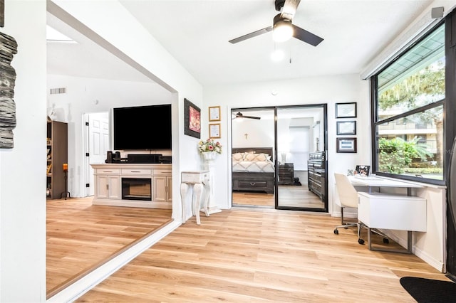 unfurnished office with ceiling fan, light hardwood / wood-style flooring, built in desk, and a fireplace