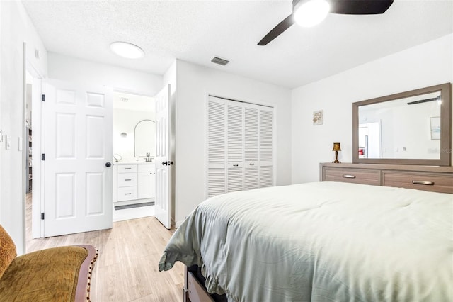 bedroom featuring light hardwood / wood-style flooring, a closet, ensuite bath, a textured ceiling, and ceiling fan