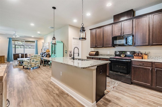 kitchen featuring light stone counters, a sink, black appliances, an island with sink, and decorative light fixtures