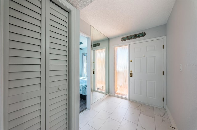 foyer entrance with marble finish floor, a textured ceiling, and baseboards