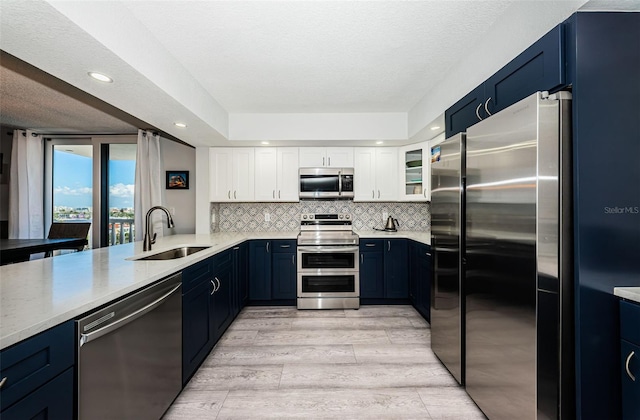 kitchen featuring light wood-type flooring, decorative backsplash, white cabinets, stainless steel appliances, and a sink