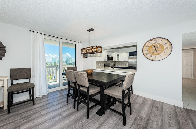 dining space with a view of city, a textured ceiling, wood finished floors, a wall of windows, and baseboards