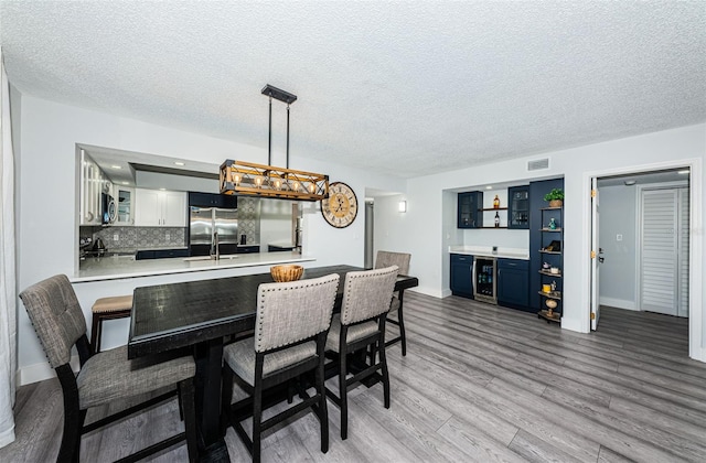 dining space with visible vents, a textured ceiling, wine cooler, a bar, and light wood finished floors