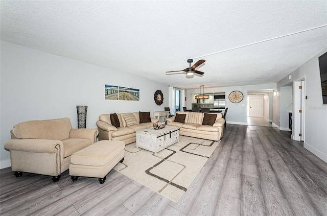 living room with a textured ceiling, a ceiling fan, baseboards, and wood finished floors