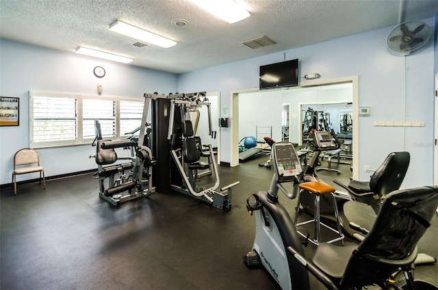 gym featuring visible vents, a textured ceiling, and baseboards