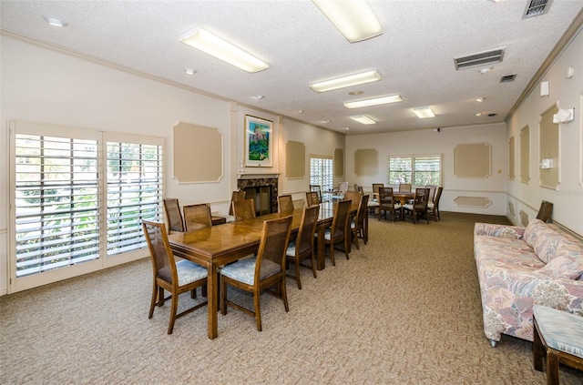 dining space featuring visible vents, ornamental molding, a textured ceiling, a glass covered fireplace, and light carpet