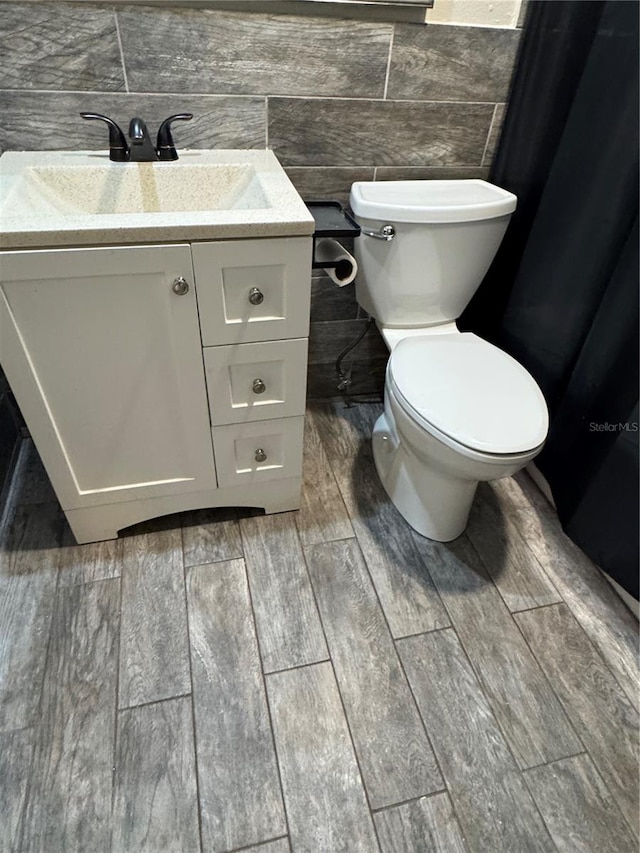 bathroom with toilet, wood finish floors, tile walls, and vanity